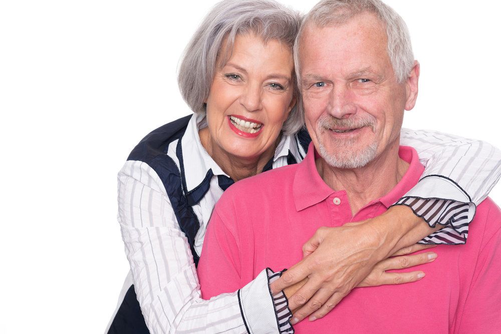 Senior couple smiling, in front of white background.